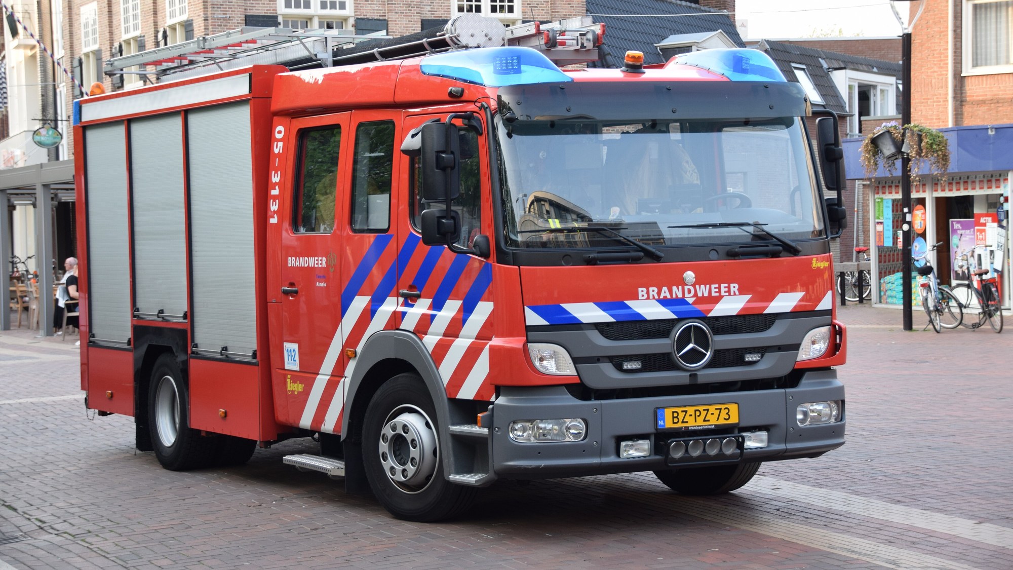 Sfeerbeeld van een rode Nederlandse brandweerwagen met blauwe zwaailichten op een straat met klinkers