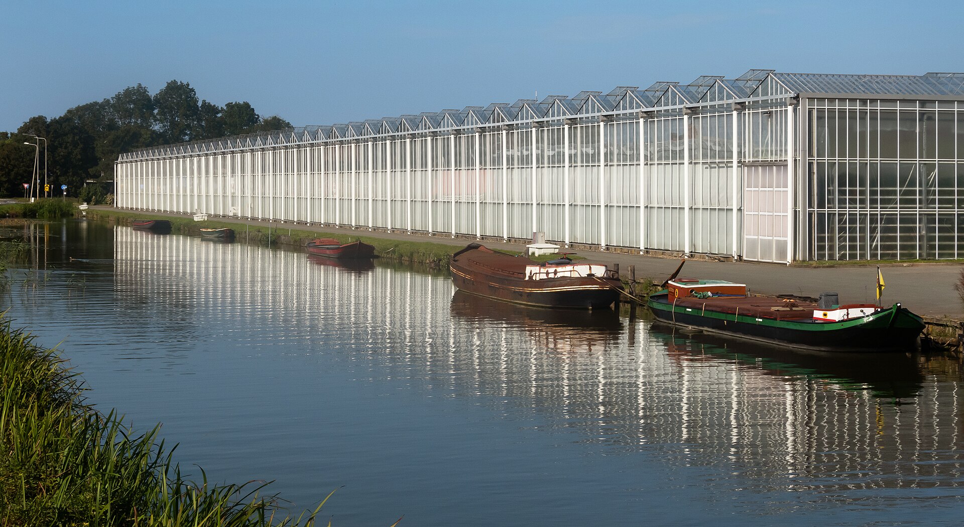 Grote tuinbouwkassen aan het water met bootjes aan de kant