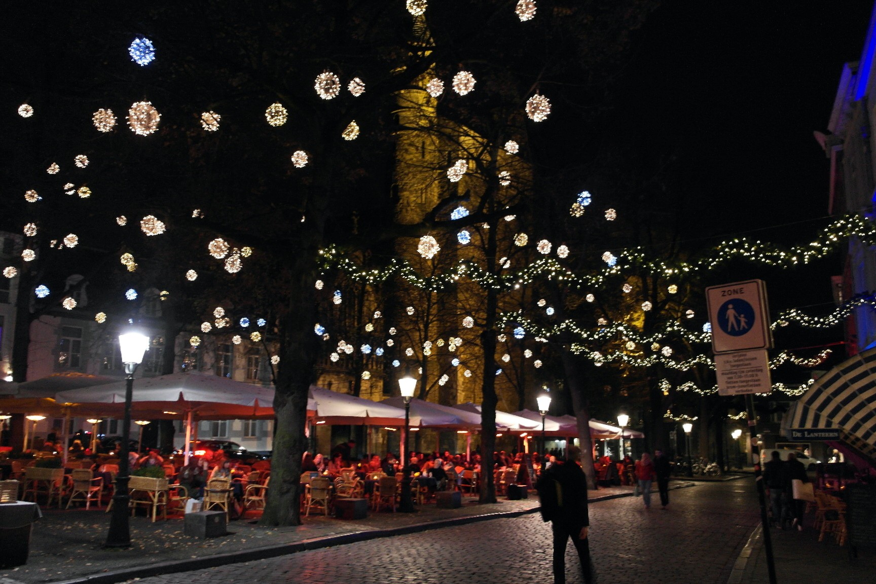 Plein met kerstverlichting in de bomen en verlichte terrassen op een winteravond