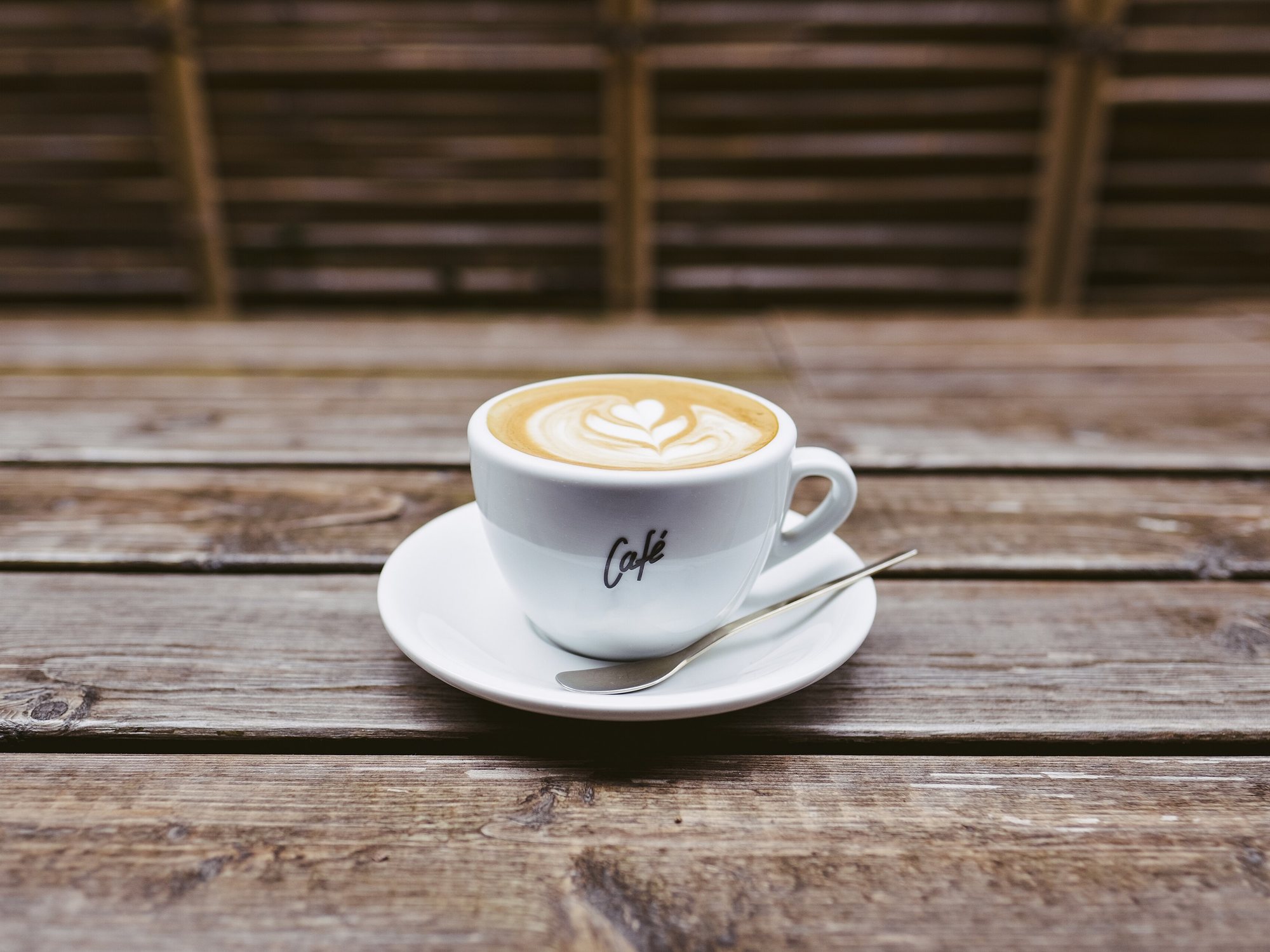 Kopje koffie met latte art op een schoteltje op een houten tafel