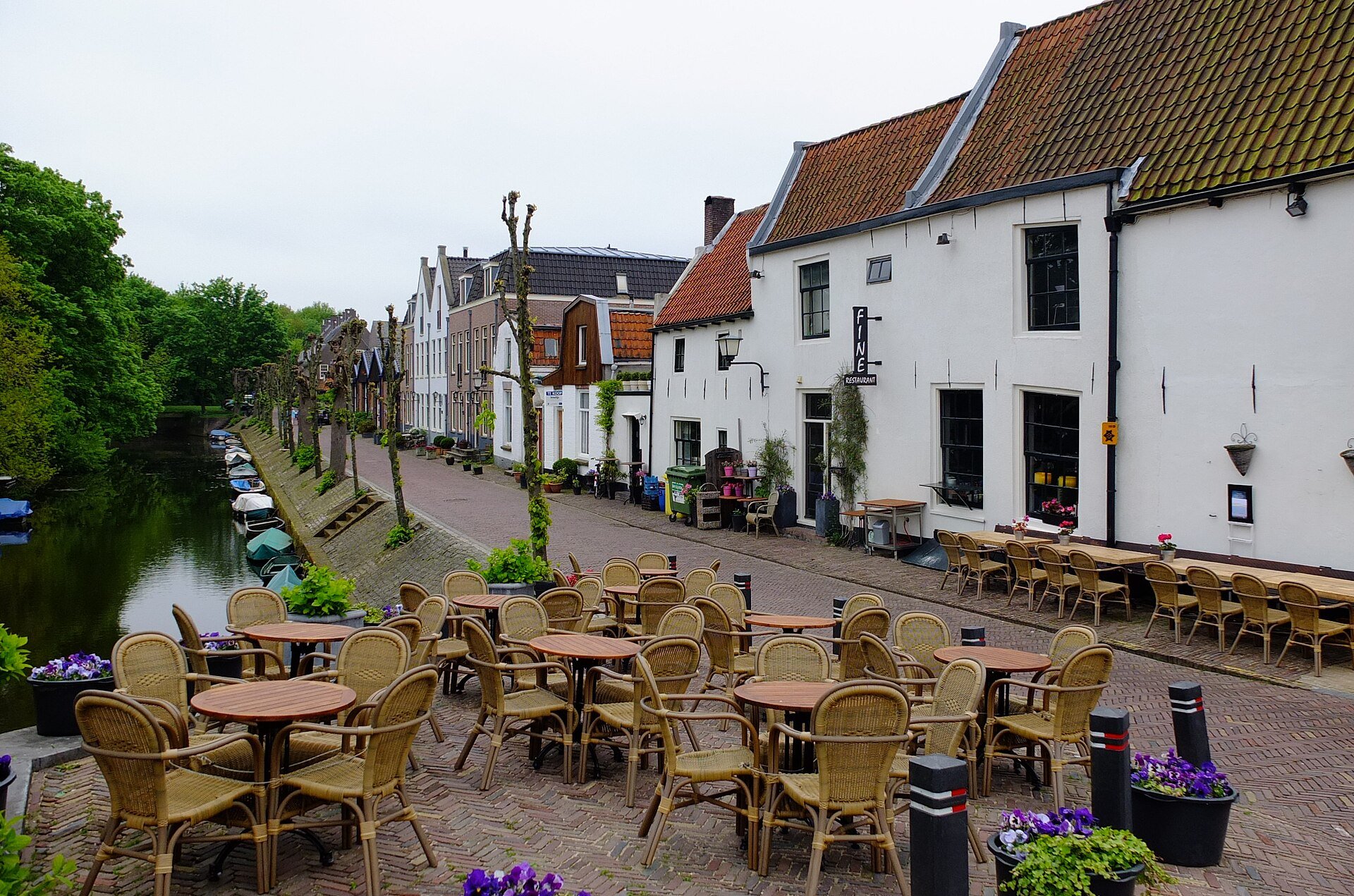Leeg terras met rieten stoelen en ronde tafels voor een restaurant aan het water