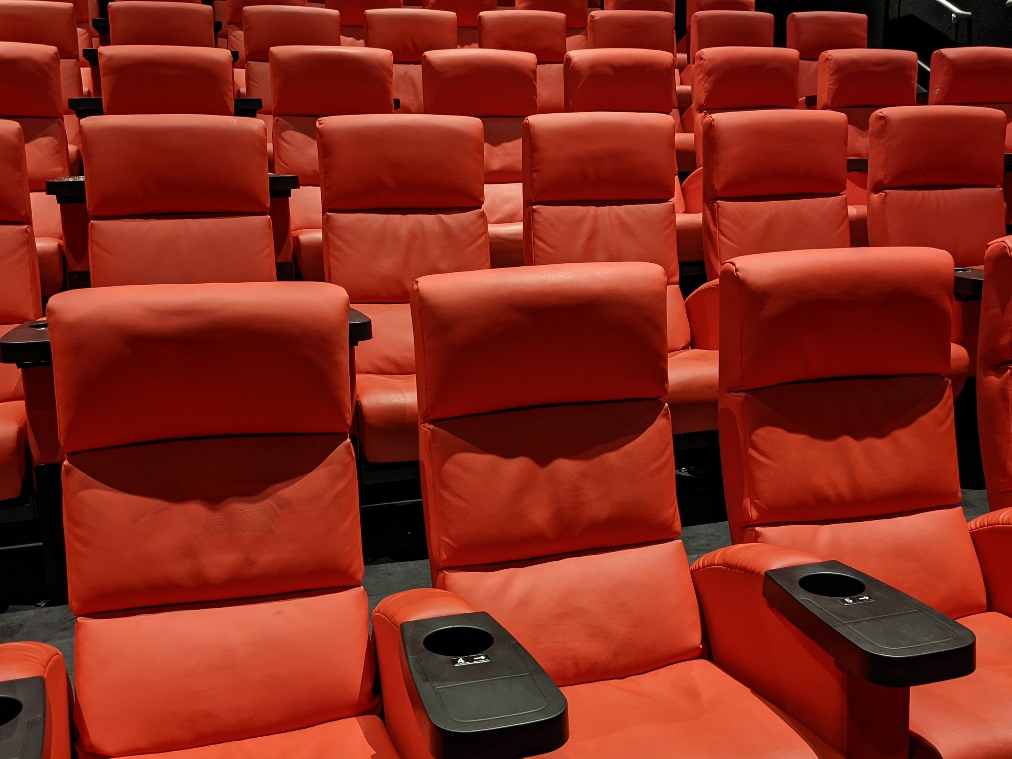 Rijen lege rode bioscoopstoelen met zwarte armleuningen en bekerhouders in een filmzaal