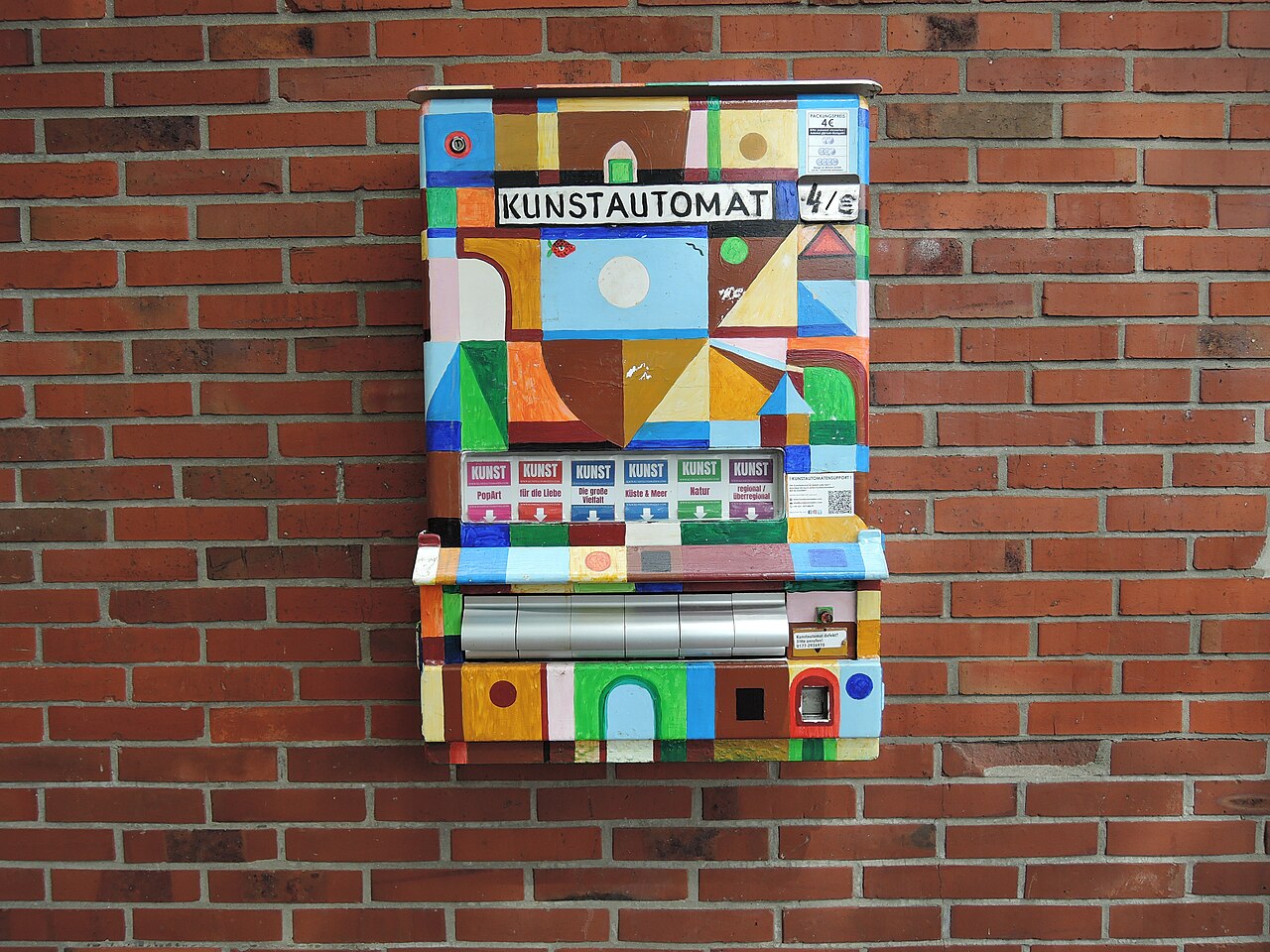 Kleurrijk beschilderde kunstautomaat aan een bakstenen muur in Stade, ter illustratie bij Pakje Kunst in Casa Cadanza