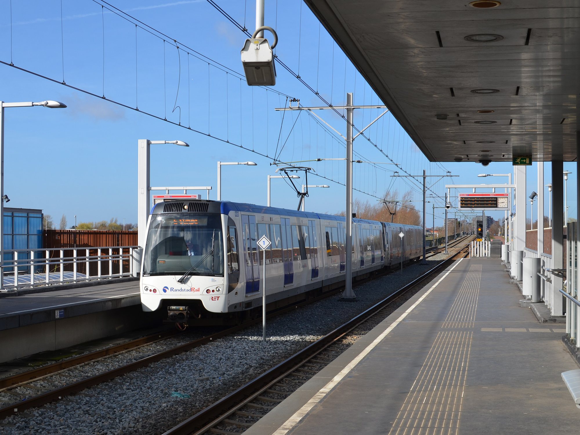 Een metro van RandstadRail rijdt metrohalte Berkel Westpolder in Berkel en Rodenrijs binnen, met een leeg perron en overkapping