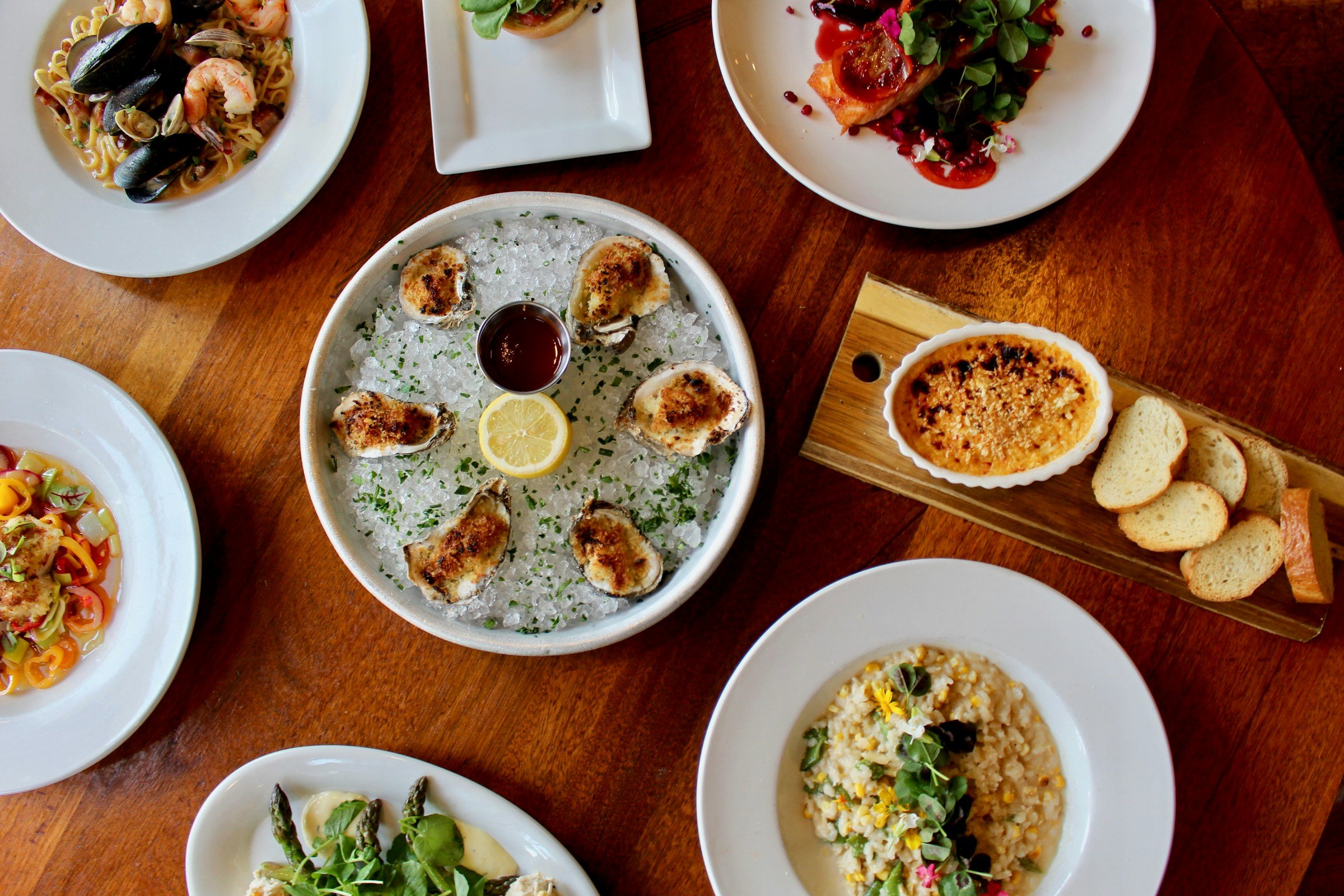 Houten restauranttafel met borden pasta, risotto, oesters, creme brulee en brood
