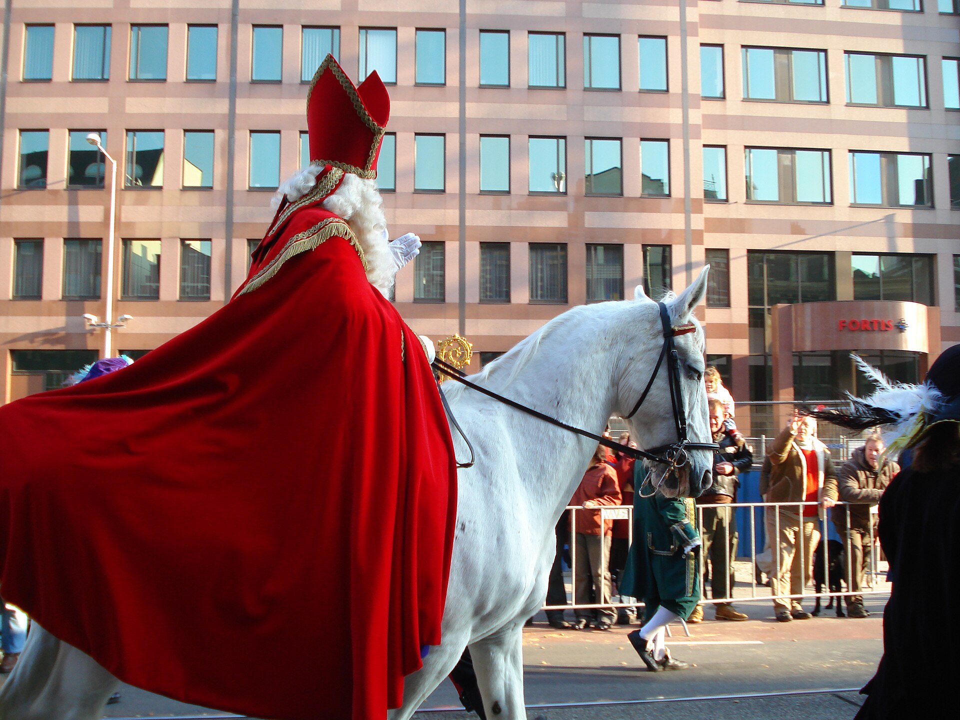 Sinterklaas op zijn witte paard tijdens een intocht, met publiek achter de dranghekken