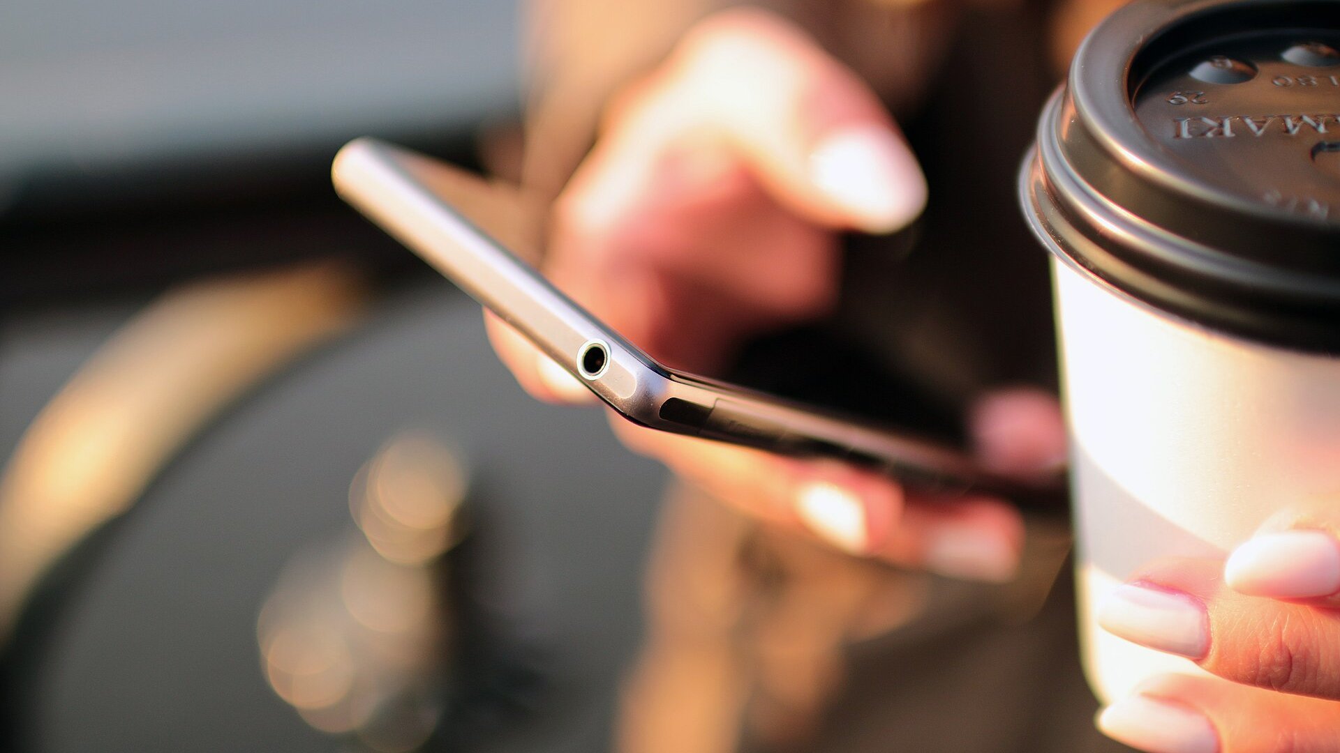 Hand met een smartphone naast een beker koffie